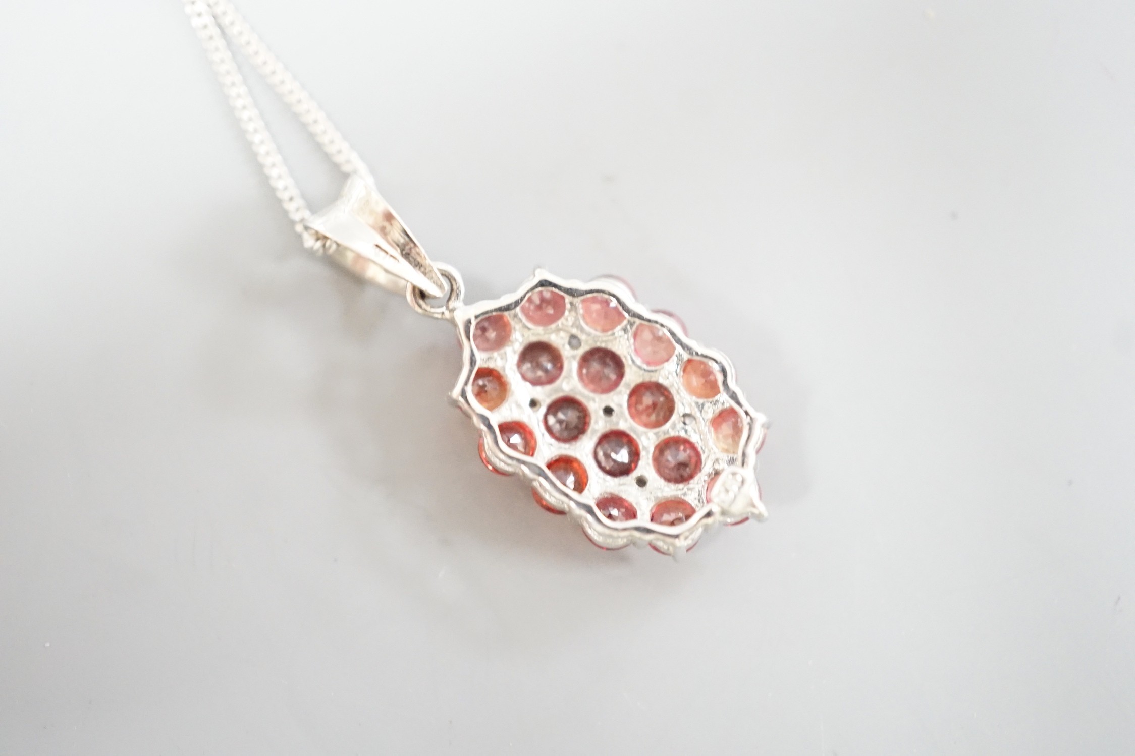 A modern 375 white metal, sunset ruby and white sapphire set cluster pendant, 19mm, on a 375 white metal chain, 42cm, gross 4 grams, with Rocks & Co certificate.